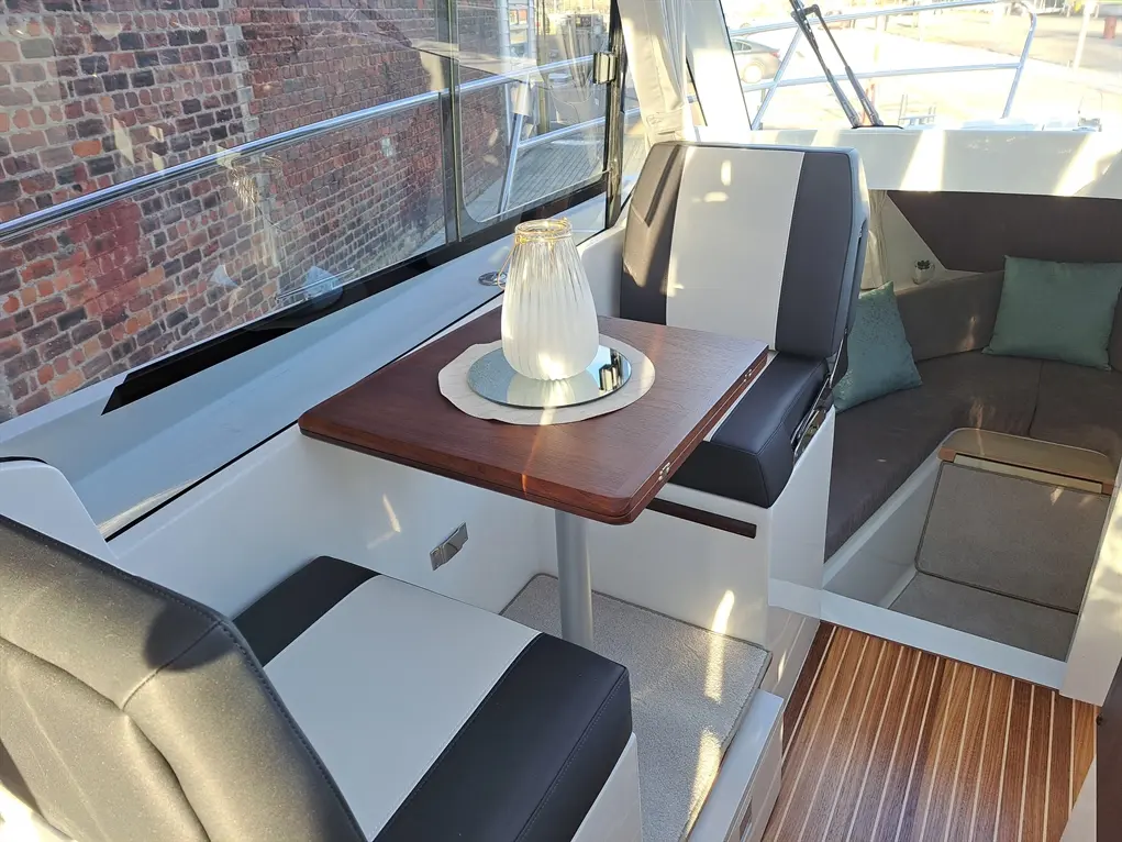 Interior of a boat featuring sleek seating, a wooden table, a decorative vase, and soft cushions against a brick wall backdrop.